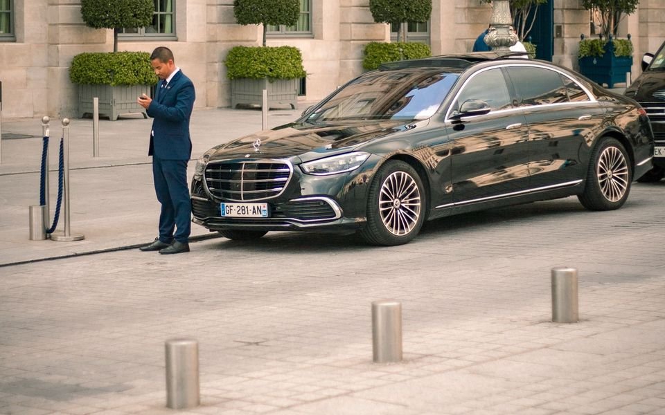 Chauffeur privé en costume à côté de sa berline